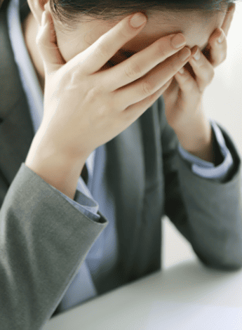 A woman in a suit is sitting with her hands over her face in distress.